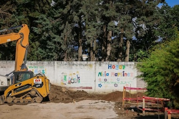 Una excavadora amarilla en un terreno de tierra con árboles al fondo y un contenedor modular blanco
