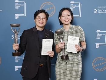 Dos mujeres sonrientes sostienen trofeos plateados y libros blancos titulados "Taiwan Travelogue" frente a un fondo azul con logos del Booker Prize