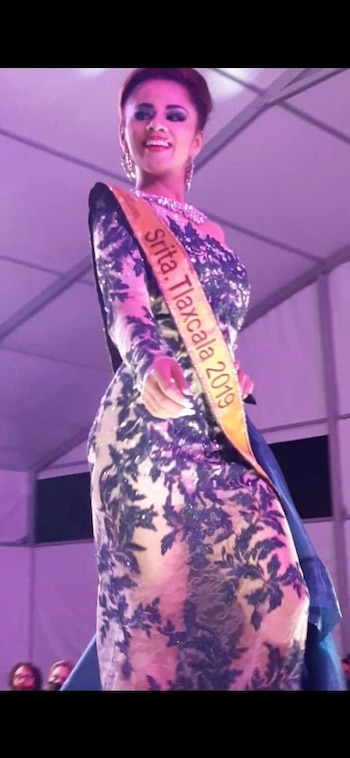 Una mujer con vestido de noche y una banda con el texto Señorita Tlaxcala 2019 camina en una pasarela con iluminación morada