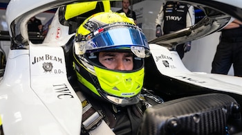 Primer plano de un piloto en la cabina de un coche de carreras blanco, con casco amarillo, negro y azul, y logos Cadillac, Tommy Hilfiger, Venezuela, Jim Beam e IWC.