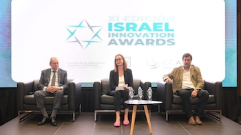 Tres personas, dos hombres y una mujer, sentadas en sillones negros sobre un escenario. Detrás, una gran pantalla muestra el logo "Israel Innovation Awards"