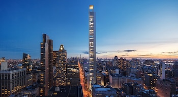 Vista aérea de un rascacielos alto y delgado en el centro de Nueva York al anochecer, con luces encendidas en los edificios y la calle iluminada