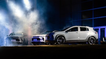 Tres vehículos Chevrolet Sonic B-SUV en un escenario oscuro con focos y humo; uno blanco a la derecha, dos oscuros al fondo