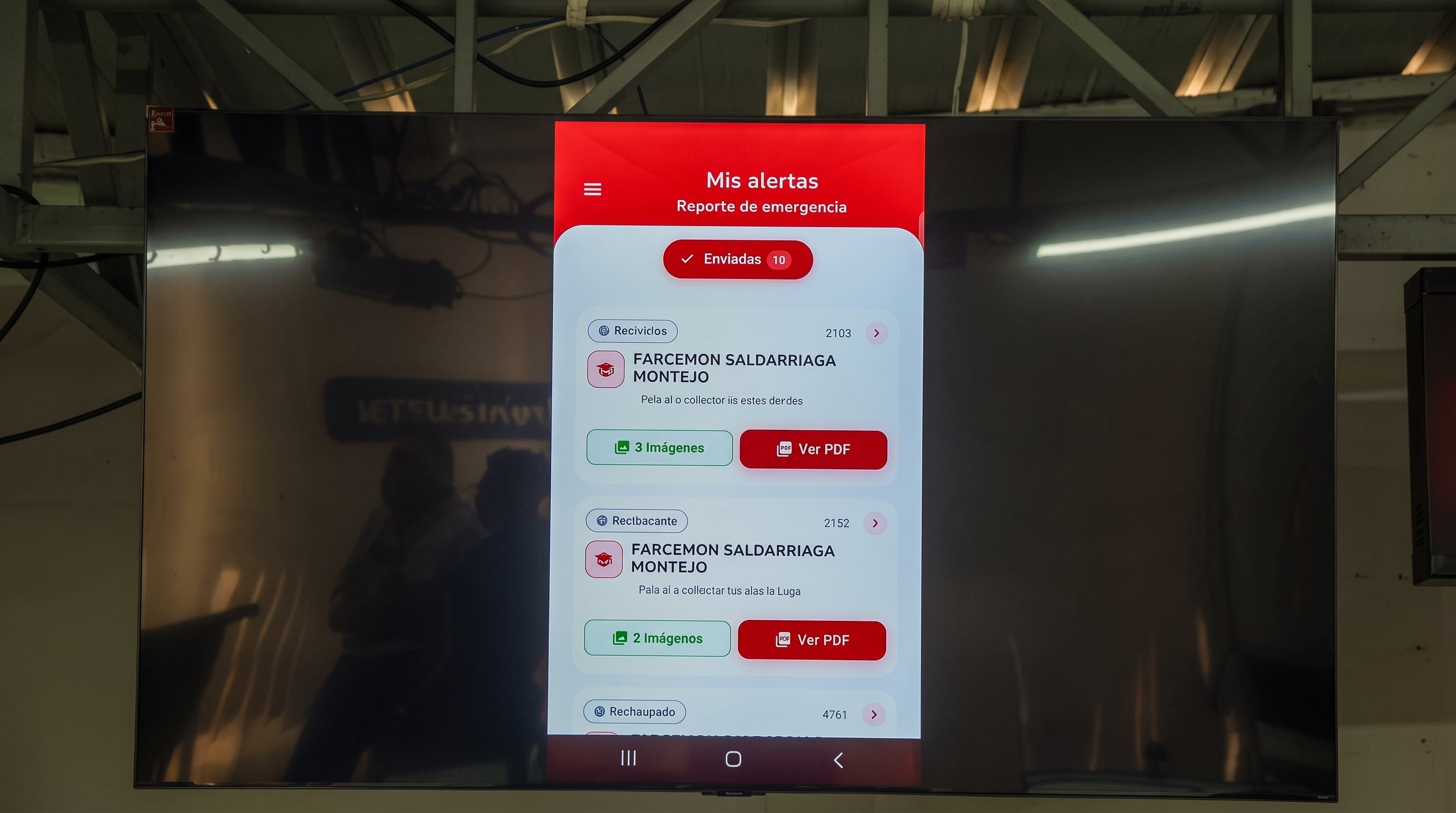 Una pantalla de televisión proyecta la interfaz de una aplicación móvil de reportes de emergencia. (Imagen Ilustrativa Infobae)