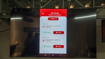 Un televisor muestra la interfaz de una aplicación móvil con el título Mis alertas y botones de reportes.