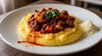 Un plato blanco con polenta amarilla cubierta con tuco rojo con carne y verduras, adornada con perejil fresco y queso rallado al lado.