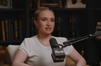 Hayden Panettiere, con cabello rubio recogido y blusa blanca, habla frente a un micrófono de podcast en un estudio