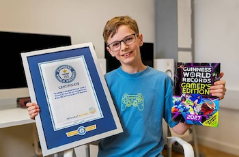 Un niño con anteojos y camiseta azul sostiene un certificado de Guinness World Records enmarcado y un libro colorido