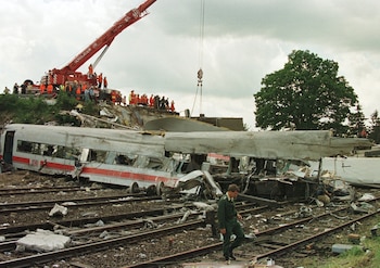 Vagones de tren destrozados sobre varias vías de ferrocarril, grúa roja, equipo de rescate, un hombre con uniforme verde camina sobre los rieles