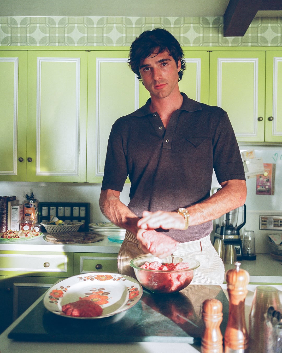 El actor Jacob Elordi, conocido por su papel como Nate Jacobs en Euphoria, prepara carne picada en una cocina vibrante con gabinetes verdes. (HBO Max)