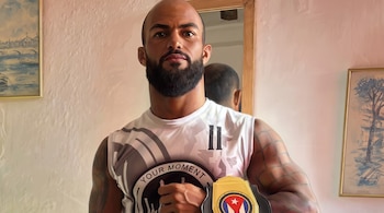 Ilustración de un hombre calvo con barba y camiseta deportiva que sostiene un emblema con los colores de la bandera de Cuba.