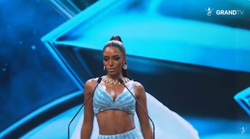 Una mujer con un traje brillante de dos piezas color azul claro habla ante dos micrófonos sobre un escenario azul