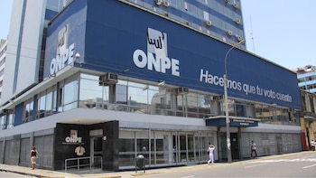 Edificio azul y blanco con el logo y el nombre ONPE, y el lema 'Hacemos que tu voto cuente' en la fachada. Personas en la acera