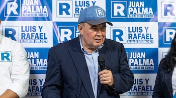 Hombre con gorra y traje sostiene micrófono. Panel político con logos "R", "Juan Palma Alcalde de Surco" y "Luis y Rafael Alcalde de Lima 2027".