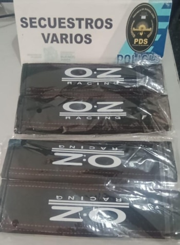 Primer plano de un cartel blanco que dice 'SECUESTROS VARIOS' y cuatro elementos negros empaquetados con el logo 'O.Z RACING' en plástico transparente