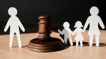Un mazo de madera se encuentra entre la figura de papel de un hombre y las figuras de un niño, una niña y una mujer sobre una mesa.