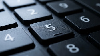 Vista macro de la tecla número 5 en un teclado numérico de computadora. Se aprecian la marca en relieve y la textura rugosa, con teclas como 2, 4, 6, 8 desenfocadas alrededor.