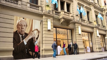 Fotografía de la fachada de un edificio con la inscripción 'Centro Cultural Borges'. Una gran imagen de Jorge Luis Borges ocupa el lado izquierdo de la fachada, con personas caminando al frente.