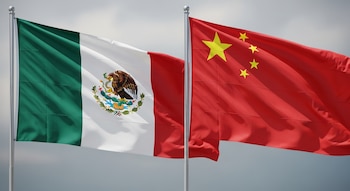 Una bandera verde, blanca y roja con un escudo central junto a una bandera roja con cinco estrellas amarillas en una composición bajo un cielo gris.