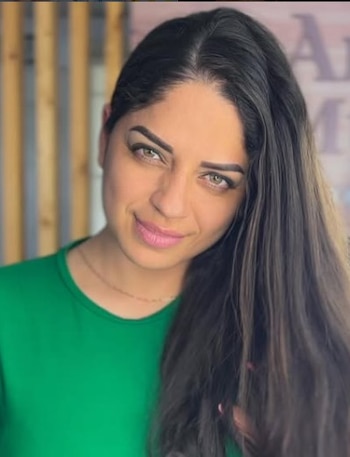 Primer plano de una mujer con cabello oscuro y largo, ojos claros, vistiendo una camiseta verde, mirando a la cámara con una leve sonrisa