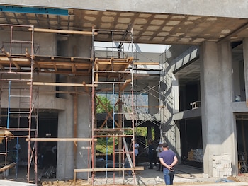 Estructuras de andamios metálicos y de madera frente a columnas de concreto en un edificio en construcción con varias personas al fondo