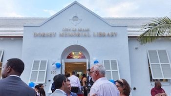 Vista exterior de la Biblioteca Conmemorativa Dorsey, un edificio blanco con techo a dos aguas y ventanas con persianas, con un grupo de personas en la entrada