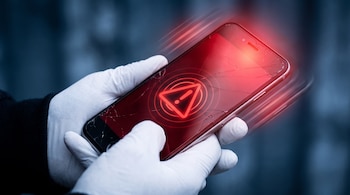 Dos manos con guantes blancos sostienen un teléfono celular con la pantalla quebrada, que emite luz roja y un símbolo de advertencia con ondas.