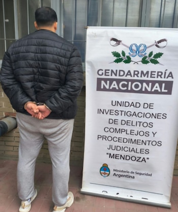 Hombre de espaldas con las manos esposadas junto a un cartel de la Gendarmería Nacional de Argentina
