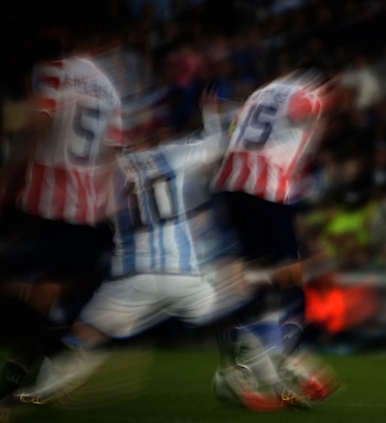 Hombre con camiseta de fútbol de Argentina con rayas celestes y blancas y el número diez, en movimiento borroso, sobre un fondo oscuro con tonos rojos