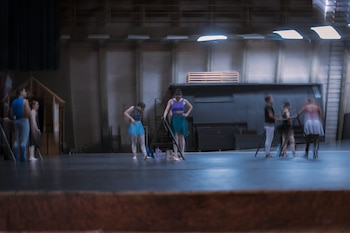 Bailarines con ropa de ensayo junto a barras de danza sobre un escenario iluminado