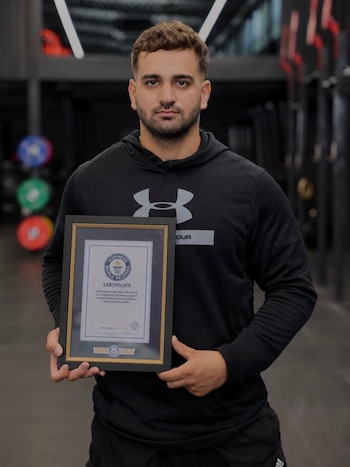 Un hombre con sudadera negra sostiene un certificado enmarcado de Guinness World Records en un gimnasio