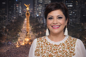 Primer plano de mujer con blusa bordada y aretes de borlas, sonriendo. De fondo, el Ángel de la Independencia iluminado y una multitud de personas.