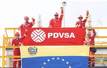 Cinco hombres con uniformes rojos y cascos de seguridad sostienen una bandera de PDVSA y la bandera de Venezuela, la mayoría con el puño en alto