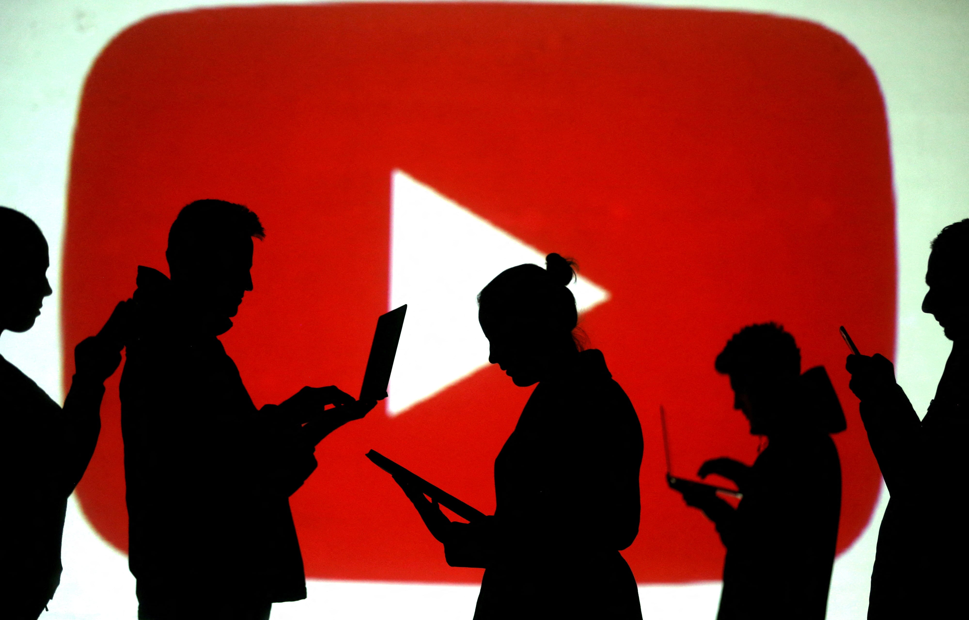 FILE PHOTO: Silhouettes of laptop and mobile device users are seen next to a screen projection of the YouTube logo in this picture illustration taken March 28, 2018. REUTERS/Dado Ruvic//File Photo