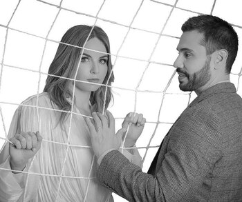 Imagen en blanco y negro de un hombre y una mujer, con una red entre ellos. La mujer mira al frente; el hombre la observa de perfil