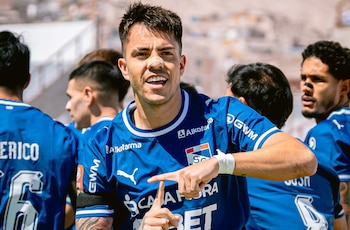 Un futbolista con una curita en la nariz y camiseta azul señala con sus dedos mientras sonríe junto a otros jugadores en la cancha