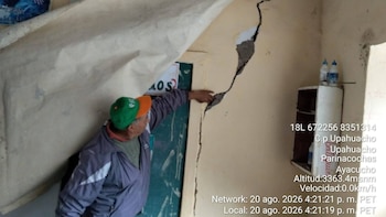 Un hombre con gorra verde señala una grieta profunda en la pared amarilla de una habitación junto a una puerta verde