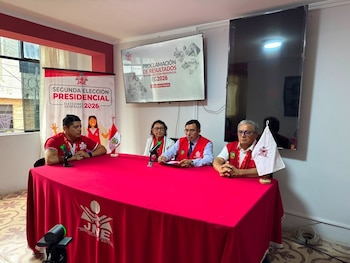 Cuatro personas sentadas a una mesa roja. Dos banderas, micrófonos y carteles del JNE con texto "Segunda Elección Presidencial". Una pantalla muestra "Proclamación de Resultados"