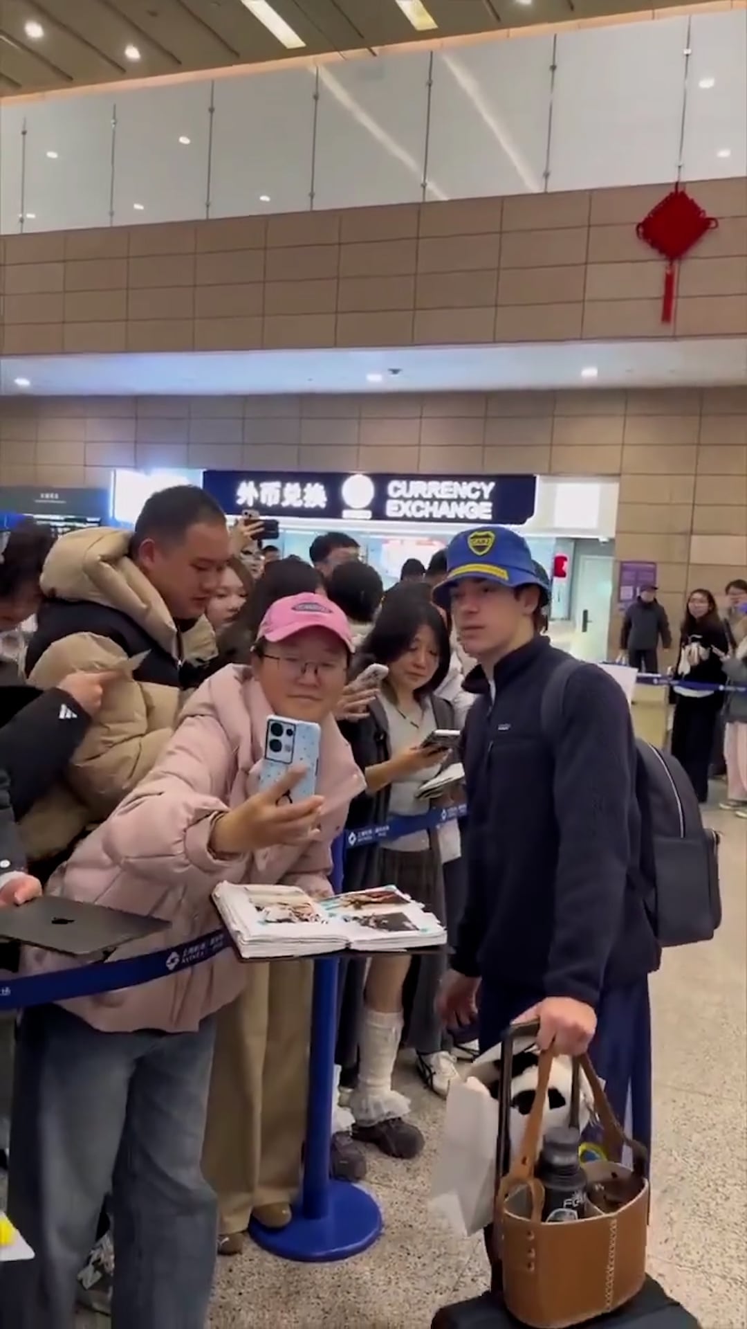 El piloto argentino Franco Colapinto llega al aeropuerto de China para el Gran Premio de F1, donde es recibido con entusiasmo por un grupo de aficionados que buscan una foto.