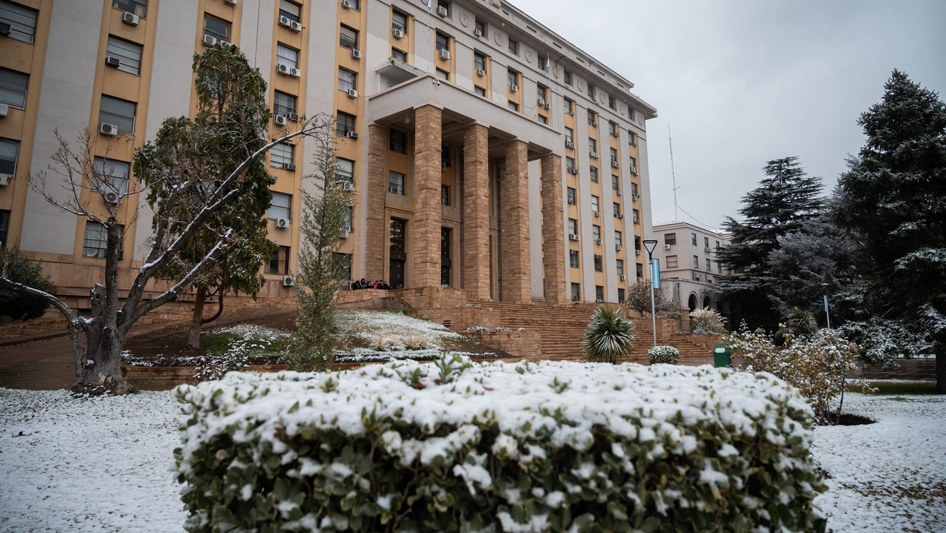 El frente de un edificio de grandes columnas de piedra, con escalinatas y un jardín, aparece cubierto de nieve en Mendoza, en el contexto de una ola polar.