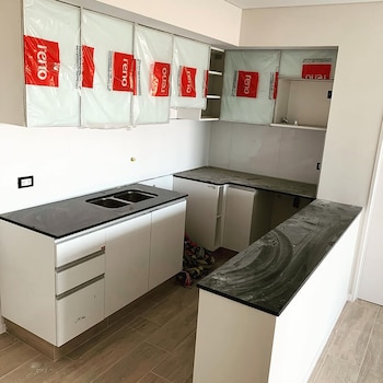 Cocina moderna con gabinetes blancos y encimeras negras. Los gabinetes superiores están cubiertos con plástico protector con el logo rojo de Reno Amoblamientos
