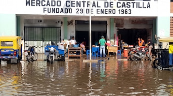 Calle anegada frente a la fachada del Mercado Central de Castilla con mototaxis, motocicletas y personas cerca del ingreso