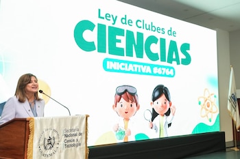 Un joven inclinado mira por un microscopio óptico frente a una mesa con rocas, frascos y una computadora portátil