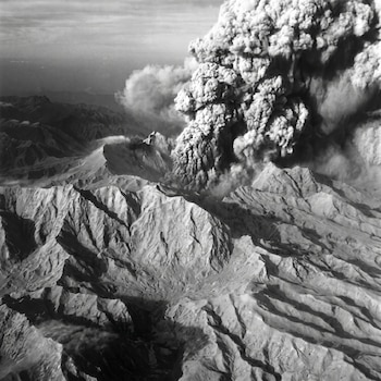 Vista aérea en blanco y negro de una enorme columna de ceniza y humo elevándose sobre el volcán Pinatubo y el desolado paisaje montañoso circundante.