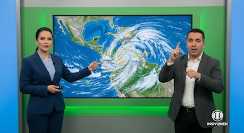 Una mujer y un hombre frente a una pantalla grande que muestra un mapa meteorológico de Centroamérica con un huracán. El hombre usa lengua de señas.
