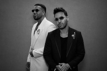 Fotografía en blanco y negro de Romeo Santos con un traje claro y Prince Royce con un traje oscuro, ambos vistiendo gafas de sol