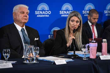 Una mujer habla por micrófono en una mesa junto a un hombre en traje, ante un fondo azul con la frase Senado Argentina