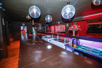 Interior de una discoteca oscura con una larga barra de madera, múltiples bolas de discoteca en el techo y luces de neón rojas en las paredes