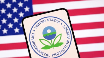 Primer plano del logo circular de la Agencia de Protección Ambiental (EPA) de Estados Unidos en una pantalla de teléfono, con la bandera estadounidense desenfocada detrás