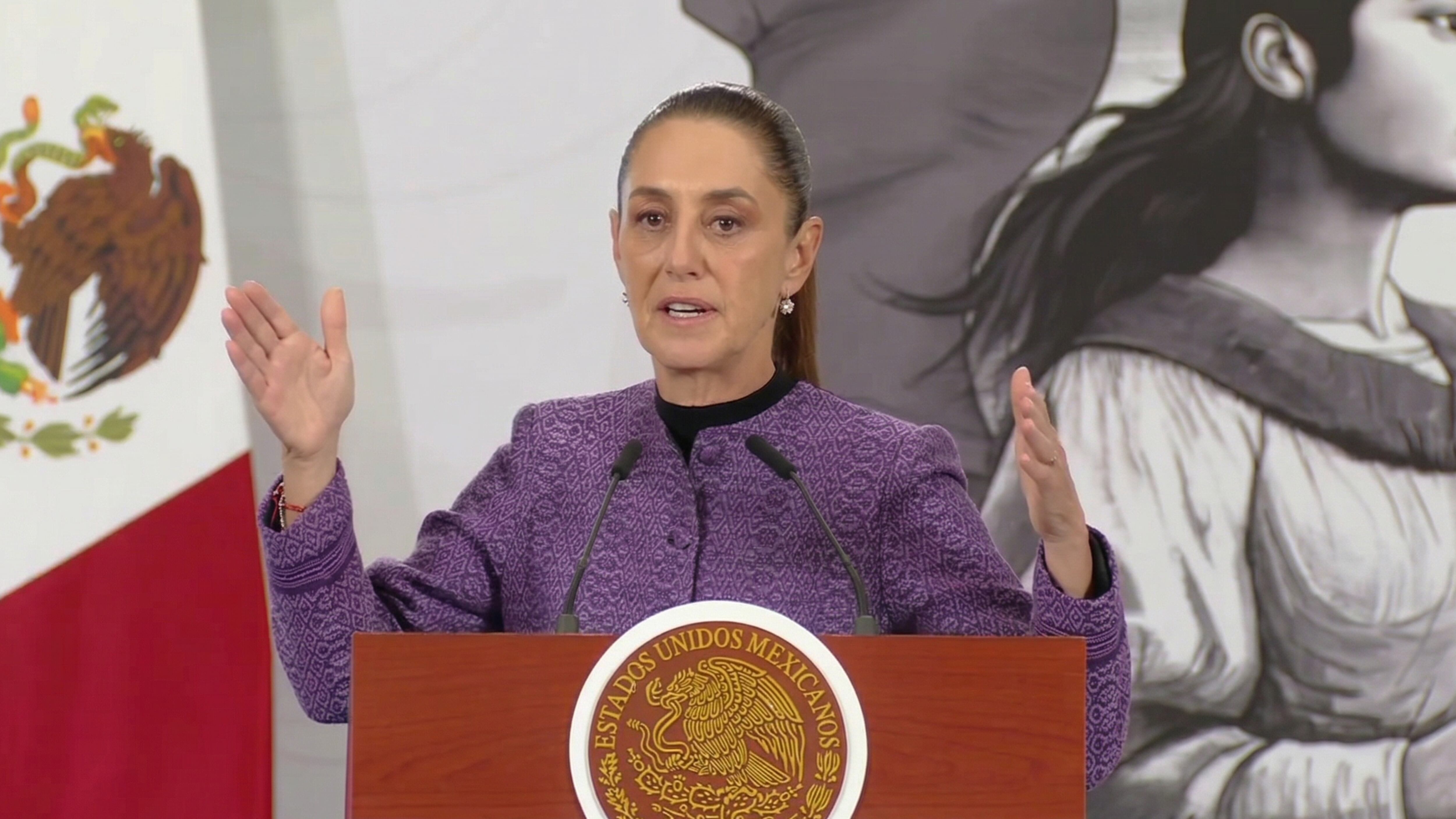 Claudia Sheinbaum Pardo pronuncia un discurso en un evento público, con el escudo nacional de México en el podio y la bandera mexicana al fondo, abordando temas relevantes para el país. (Captura de pantalla )